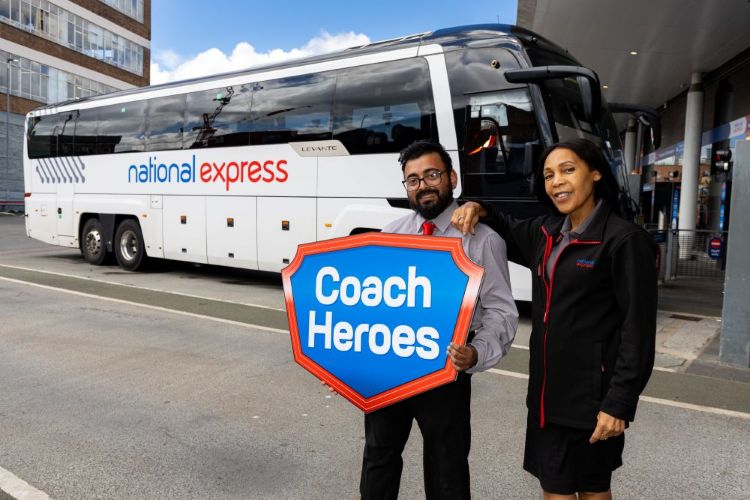 2 employees holding a sign reading "coach heroes" in-front of a white coach